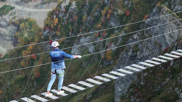 Young Happy Female Tourist Walking on Rope Bridge Hanging on Top of Mountain. Adventurer and Lover