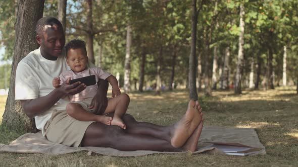 African-American Father and Son Resting under Tree in Park