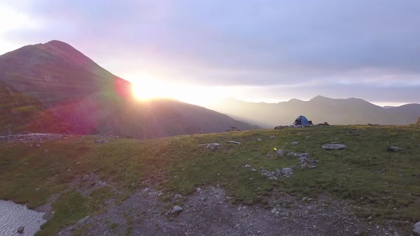 Descending drone view at sunset with cloudy sky and tent on ridge with view of Negoiu in the distanc