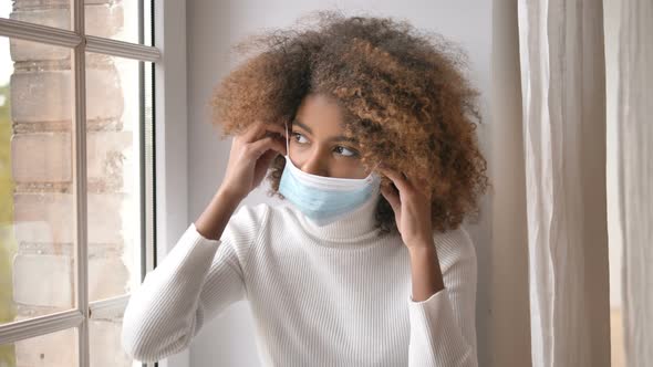 Sad Young Woman with Dark Skin Puts on Protective Blue Mask