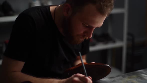 Tracking Shot of Bearded Shoemaker Painting Heel and Sole of Light Brown Leather Shoes with Brush