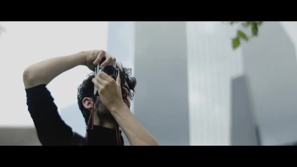 Caucasian man with beard focusing with his camera and taking pictures in the city