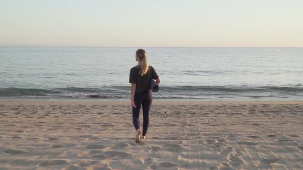 Female yogi walking towards the sea with yoga mat