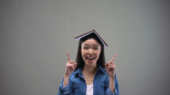 Smiling Woman With Book on Head Pointing Fingers Up, University Advertisement