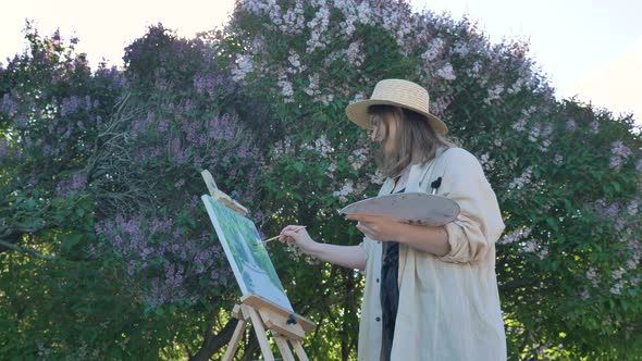 Young Woman Painter in Straw Hat and Shirt Paints By Lilac