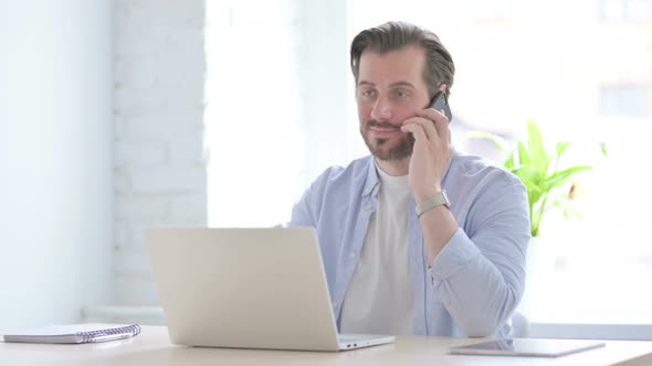 Young Man Talking on Phone While Using Laptop