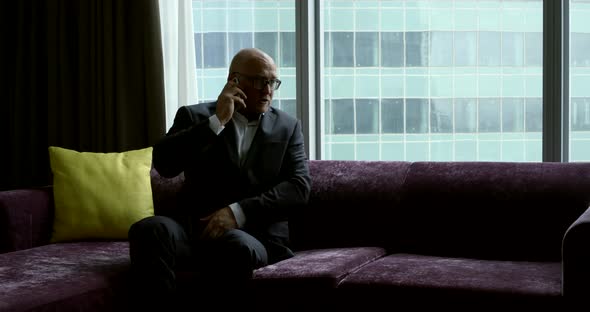 Adult Successful Man Is Talking By Cell Phone Sitting Alone on Large Couch and Resting