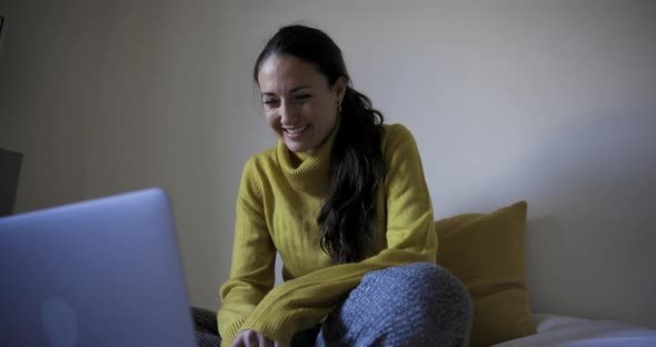 Happy woman with laptop computer on the bed watching movie and navigating onl