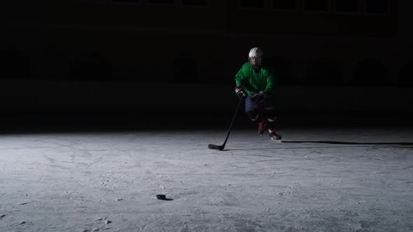 Forward in Green Uniform with Stick in Hands Slides on Ice and Hitting Puck