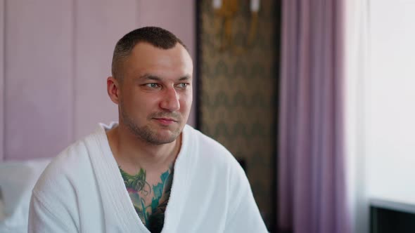 Angry Man Grimaces Sitting on Bed in Hotel Room Closeup