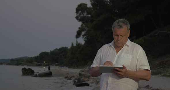 Senior man using tablet PC on beach in late evening