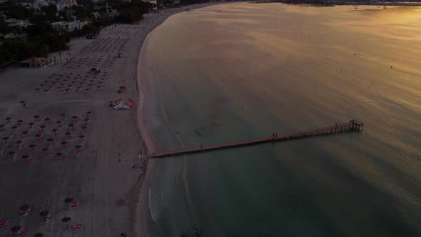 Aerial View of Playa de Alcúdia, Mallorca during Sunrise with Pier and Mountains in Background