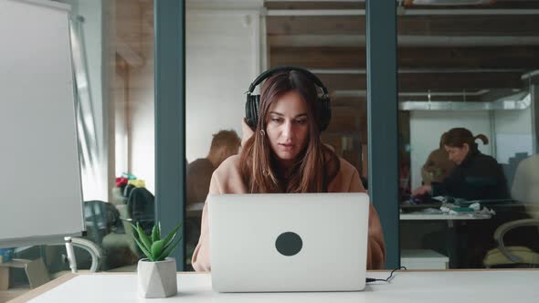 Portrait of Happy Woman Businessperson Young Student in Headphones Looks at Laptop Screen Reads Good
