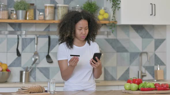 African Woman Making Online Payment on Smartphone in Kitchen