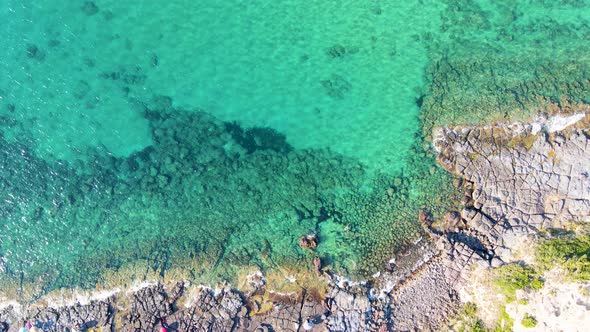 Tracking shot aerial drone view of coastline with people sunbathing and relaxing