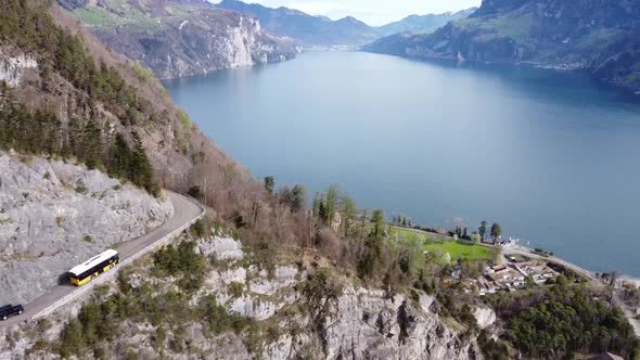 a typical yellow swiss post bus drives on a mountain road in front of the picturesque urnersee (lake