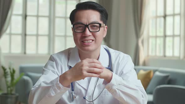 Asian Male Doctor Sit At Desk In Home Office Consult Client Online