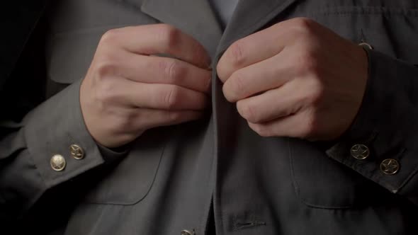 Closeup of Hands Fastening Buttons on a Gray Uniform