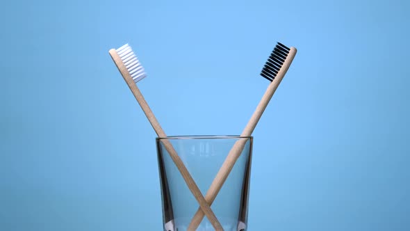 Bamboo Toothbrushes Rotating in Glass on Blue Background