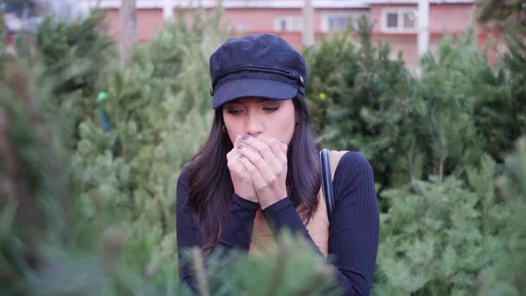 A young woman shopping for a Christmas tree and looking cold in the winter holiday season.