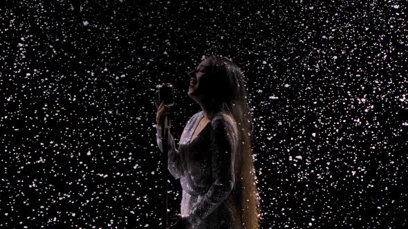 Silhouettes of a Beautiful Singer with a Vintage Microphone Against the Background of Falling Snow