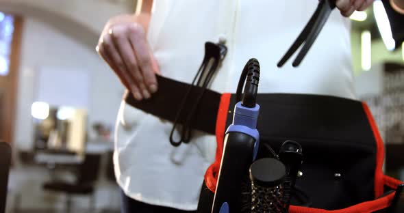 Mid-section of female hairdresser removing equipments from waist bag