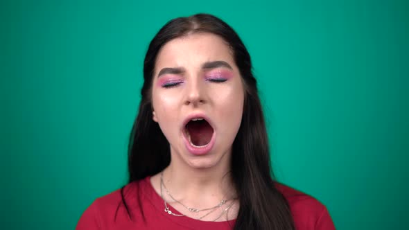 Young Tired Woman Yawning Looking at Camera Isolated on Blue Background