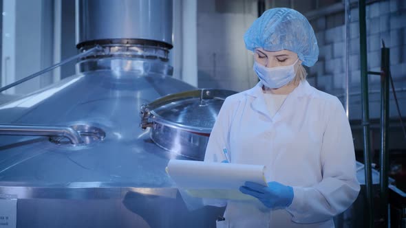 Woman Writes in Papers Standing Near Shiny Metal Tank