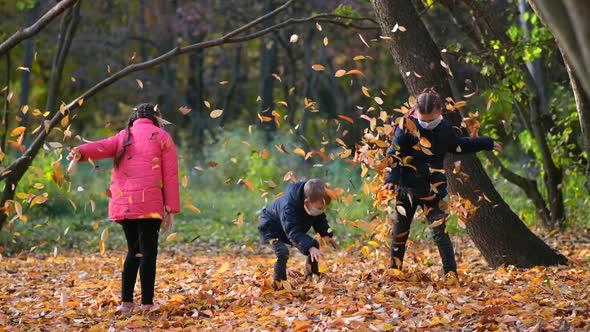 Small children in medical masks throw fallen yellow leaves in the Park on an autumn day. 