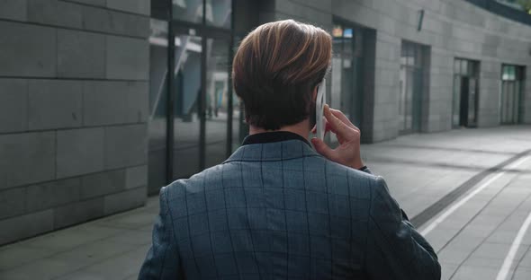 Rear View of Ambitious Businessman Talking on Mobile Phone and Walking Through the Business District