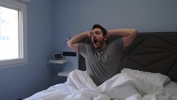 Young latin man yawning and stretching in bed after sleeping.