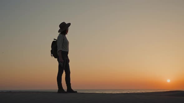 Young tourist with a retro camera looking at the sea at sunset