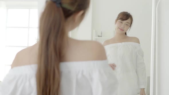 Beautiful asian young woman smiling dressing looking on mirror at bedroom.