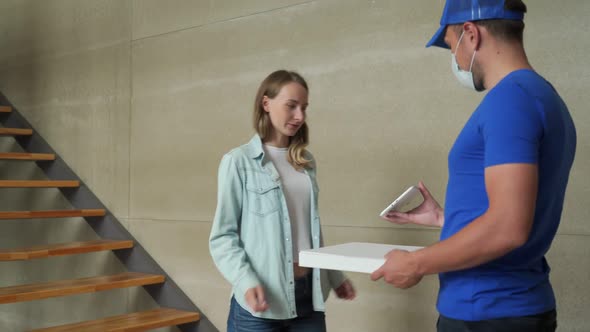 Friendly Pizza Delivery Guy in Protective Medical Mask Handing Order To Customer at Home