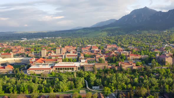 Aerial pan up reveal of beautiful flatiron mountain vista, bright green trees, and CU Boulder campus