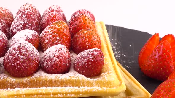 Belgian waffles with strawberry and powdered sugar on a stone board on a white background