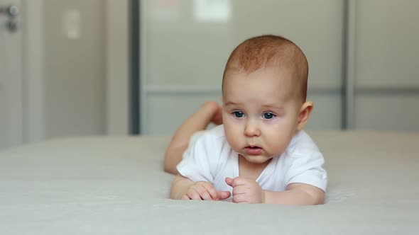 Cute Baby Lies on Bed Looking in the Camera and Smiling