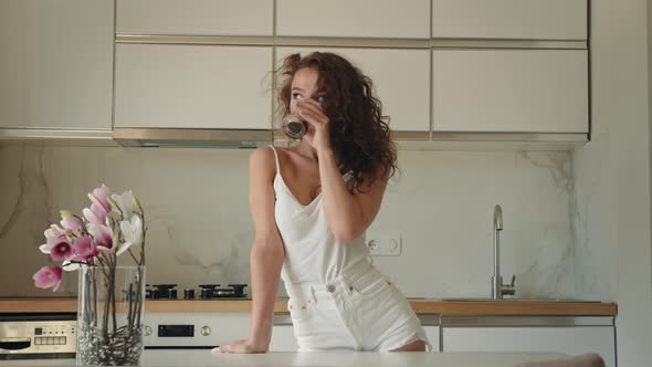 A Young Woman is Standing in the Kitchen and Drinking Coffee