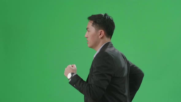 Side View Of Asian Business Man Walking While Looking At Watch And Run On Green Screen Chroma Key