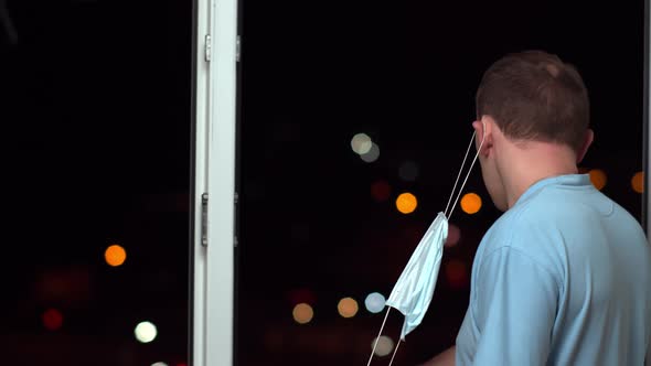 A young man breathes fresh air at night by an open window