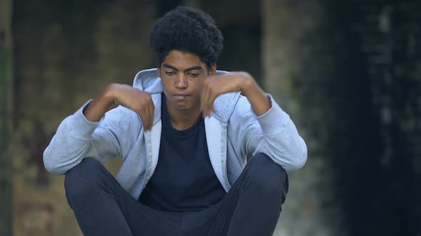 Sad Afro-American Teenager Putting on Hood Sitting Street Alone Thinking Problem