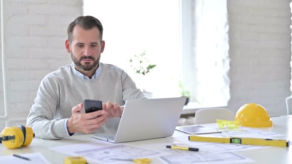 Serious Young Architect Using Smartphone in Office