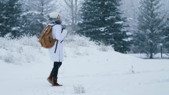 Traveler with Backpack Enjoying Falling Snow Trying to Catch Snowflake on Hand