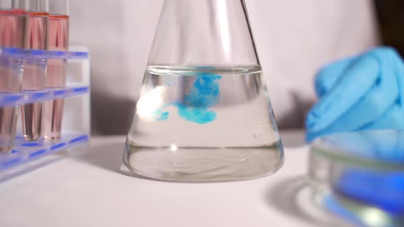 A Scientist Pours a Blue Liquid Into a Flask