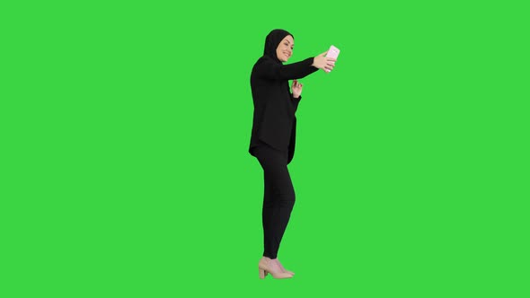 Smiling Arab Woman in Hijab Taking Selfie Pictures on Her Mobile Phone on a Green Screen, Chroma Key