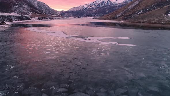 Flying over and looking down at ice layer on lake during sunset