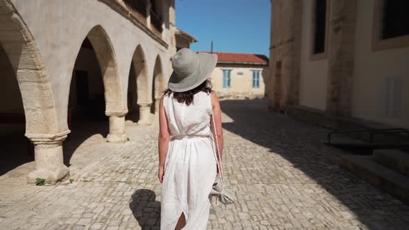 Tracking Shot of Slim Young Woman Strolling in Slow Motion Along Sunny Ancient City Street Admiring