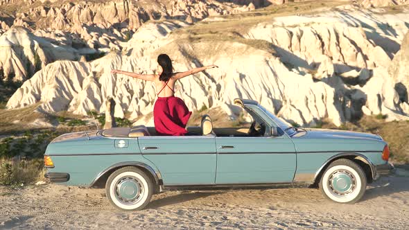 Sexy Woman in Red Dress is Watching the Sandstone Hoodoos Landscape in Old Classic Blue Car