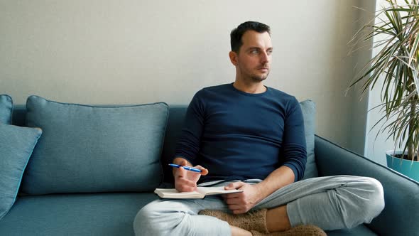 a Young Man Sits on the Couch and Takes Notes in a Notebook