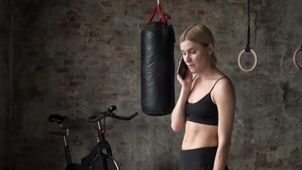 Fitness woman calling mobile phone in gym club. Young woman sitting in gym